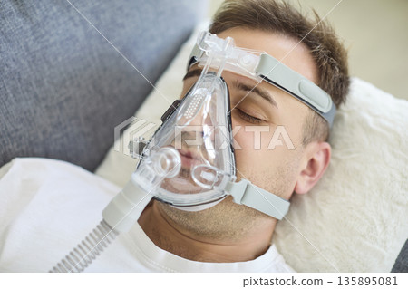 Man resting in bed with oxygen mask, receiving breathing support therapy at home Man resting in bed with oxygen mask, receiving breathing support therapy at home 135895081