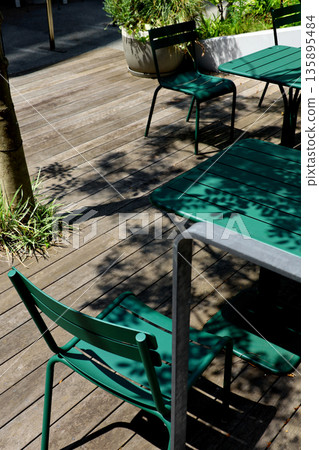 陽光透過樹木灑在木質露台和綠色的桌椅上。 135895484