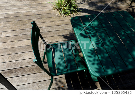 陽光透過樹木灑在木質露台和綠色的桌椅上。 135895485