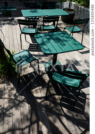 陽光透過樹木灑在木質露台和綠色的桌椅上。 135895486