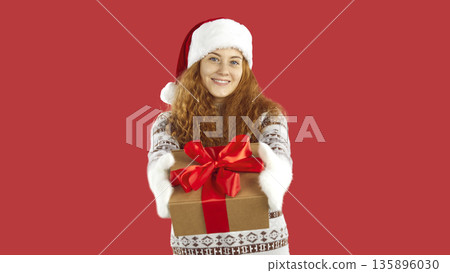 Cheerful cute young woman give you xmas present standing on red background in studio. Cheerful cute young woman give you xmas present standing on red background in studio. 135896030