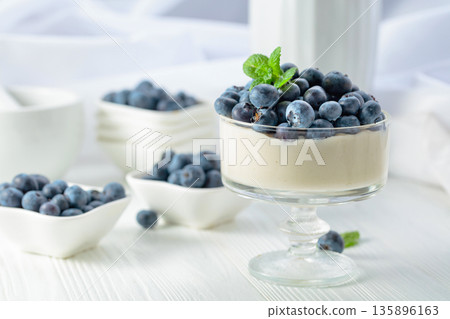 Panna cotta with fresh blueberries in a clear bowl. 135896163
