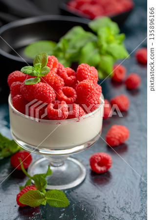 Panna cotta with fresh raspberries in a clear bowl. 135896166