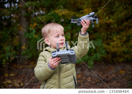 A young boy joyfully displays a drone controller in one hand and a drone in the other, surrounded by vibrant autumn foliage. A young boy joyfully displays a drone controller in one hand and a drone in the other, surrounded by vibrant autumn foliage. 135896484