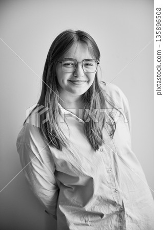 Portrait of beautiful girl smiling to camera. Cute girl in cream shirt and square glasses posing on white background. Black and white image. 135896508