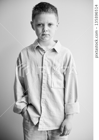 Portrait of young sad boy keeping hand in pocket, looking to the camera. Serious kid in casual clothes posing on white background. Black and white image. Portrait of young sad boy keeping hand in pocket, looking to the camera. Serious kid in casual clothes posing on white background. Black and white image. 135896514