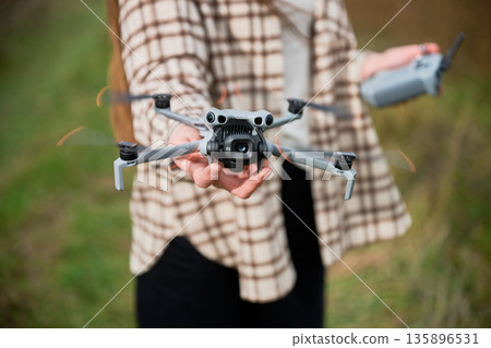 A person stands in a lush green field, grasping a high-tech drone with care. The sun casts shadows, emphasizing the excitement of capturing new views. A person stands in a lush green field, grasping a high-tech drone with care. The sun casts shadows, emphasizing the excitement of capturing new views. 135896531