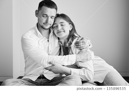 Portrait of father and teenage daughter hugging each other at home. Cute moment of dad and child in glasses showing their love to each other. Lovely spending time with family. Black and white image. 135896535