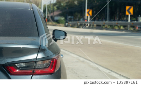 Rear side view of grey car on the concrete road. Closed on taillight of car. Driving alone on the road with traffic sign and guardrail. Clear roads and traffic. 135897161