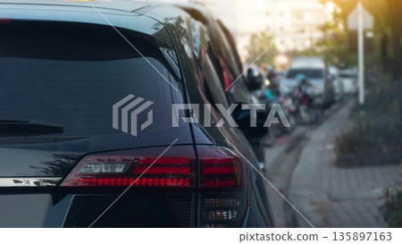 Rear side of black car parking side of road. with blurred of car and motorcycle is parked in front. sidewalks and trees in the dim light. Rear side of black car parking side of road. with blurred of car and motorcycle is parked in front. sidewalks and trees in the dim light. 135897163