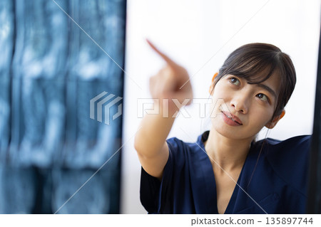 一位身穿藏藍色醫用工作服的年輕日本女子正在查看X光片。 135897744