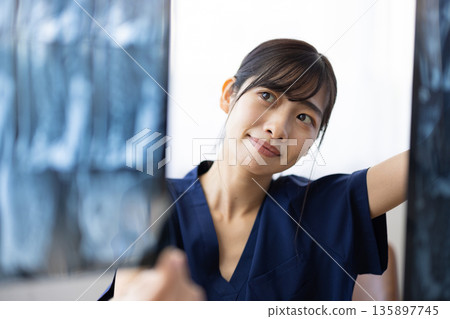 A young Japanese woman wearing a navy blue medical scrub looking at an X-ray image A young Japanese woman wearing a navy blue medical scrub looking at an X-ray image 135897745