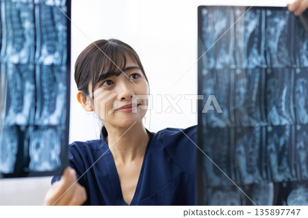 A young Japanese woman wearing a navy blue medical scrub looking at an X-ray image A young Japanese woman wearing a navy blue medical scrub looking at an X-ray image 135897747
