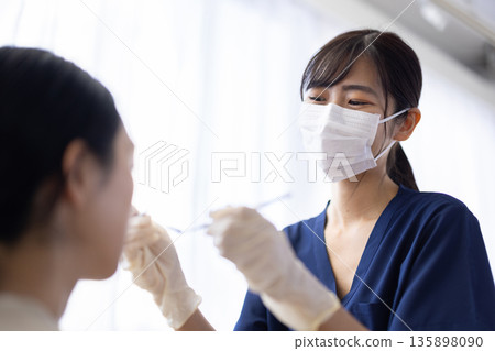 年輕的女牙醫手持牙科器械，正在檢查病人的牙齒。 135898090