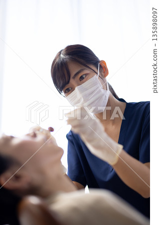 年輕的女牙醫手持牙科器械，正在檢查病人的牙齒。 135898097