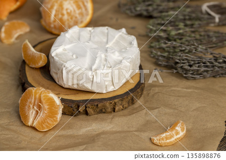 fresh white soft cheese with white mold lies on a wooden board on crumpled paper, soft round cheese and juicy sweet orange tangerines fresh white soft cheese with white mold lies on a wooden board on crumpled paper, soft round cheese and juicy sweet orange tangerines 135898876