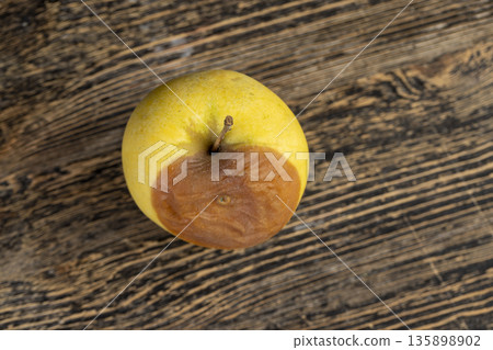 a whole yellow apple with a orange spot during rotting, one rotting apple on a black wooden table made of pine wood 135898902
