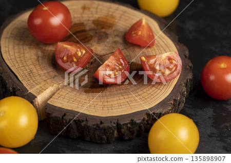 a red tomato cut into pieces and fresh and ripe tomatoes of red and yellow color scattered on the table, several tomatoes lie on a wooden board and a black slate stone 135898907