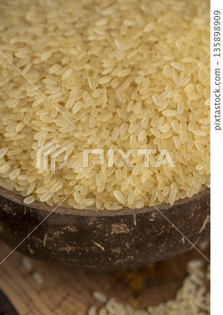 white ground dry rice, poured before cooking, poured natural pure polished rice on the table before cooking, The rice is poured into a bowl made from coconut shells white ground dry rice, poured before cooking, poured natural pure polished rice on the table before cooking, The rice is poured into a bowl made from coconut shells 135898909
