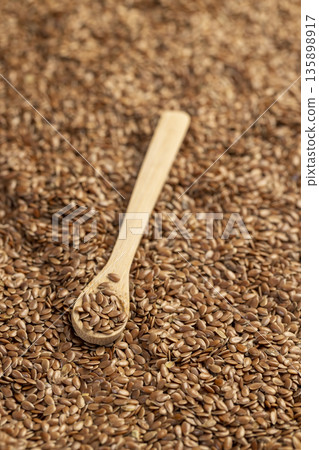 flax seeds for sowing in a wooden spoon, a large number of light brown flax seeds and a spoon with seeds 135898917