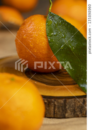 wet fresh orange small tangerines with green leaves on a wooden board and yellow paper, a group of ripe sweet tangerines with green leaves covered with drops of clear water wet fresh orange small tangerines with green leaves on a wooden board and yellow paper, a group of ripe sweet tangerines with green leaves covered with drops of clear water 135898960