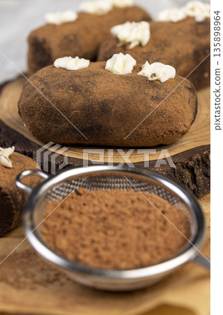 sweet brown pastry potatoes are lying on a serving board and paper, sweet classic cake from butter and a large amount of cocoa mixed with sponge cake and cognac, cocoa powder nearby 135898964