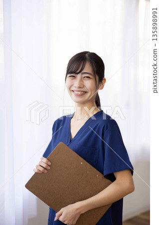 一位身穿藏藍色手術服的年輕女子，面帶微笑，手裡拿著一個文件夾。 135898991