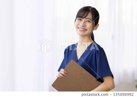 一位身穿藏藍色手術服的年輕女子，面帶微笑，手裡拿著一個文件夾。 135898992