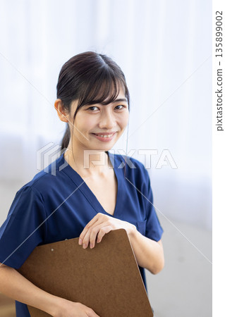 A young woman wearing navy blue scrubs and smiling while holding a binder A young woman wearing navy blue scrubs and smiling while holding a binder 135899002