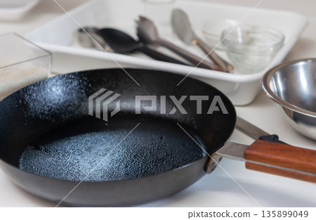 廚房檯面上擺放著一口用過的鐵煎鍋和一些烹飪用具,包括一口黑鍋、幾個碗和一把夾子。 廚房檯面上擺放著一口用過的鐵煎鍋和一些烹飪用具,包括一口黑鍋、幾個碗和一把夾子。 135899049
