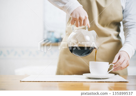 Woman pouring coffee into a coffee cup Woman pouring coffee into a coffee cup 135899537