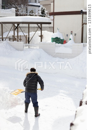 Rear view of a senior man shoveling snow with a snow shovel Rear view of a senior man shoveling snow with a snow shovel 135899615