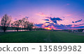 Rural landscape with beautiful evening sky at sunset. Green field and village on the horizon 135899982