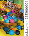 Colorful easter eggs in a basket on a yellow wooden table. Vertical photo 135900004