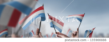 Luxembourg flags in their hands on a blurred urban background Luxembourg flags in their hands on a blurred urban background 135900886