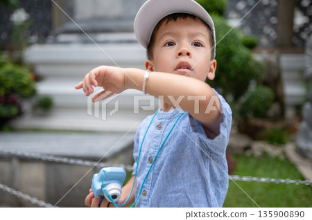 Young Boy In Cap Holds Toy Camera, Capturing Beautiful Temple Scene Young Boy In Cap Holds Toy Camera, Capturing Beautiful Temple Scene 135900890