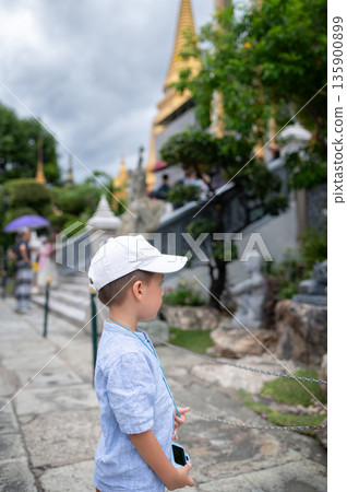 Young Boy Using Toy Camera to Photograph Statues in Lush Garden Setting in Bangkok, Thailand 135900899