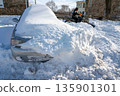 Man on ATV plows snow clearing driveway with a car buried in snowdrift 135901301