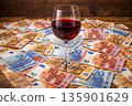 Wine glass sits on a spread of euro bills on a wooden table surface 135901629