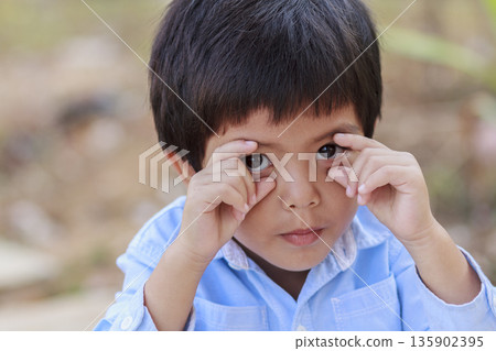 Portrait of happy cute Asian Thai little boy rounding his eyes with his fingers 135902395