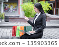 Happy young asian woman holding credit card and using laptop for online shopping in park. 135903365