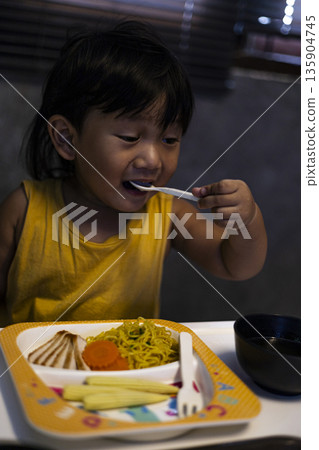 Toddler Is Eating Noodles With Soup, A warm photo of a toddler noodles with soup, steam rising in soft light, perfect for a family dining campaign or a cozy mealtime documentary. 135904745