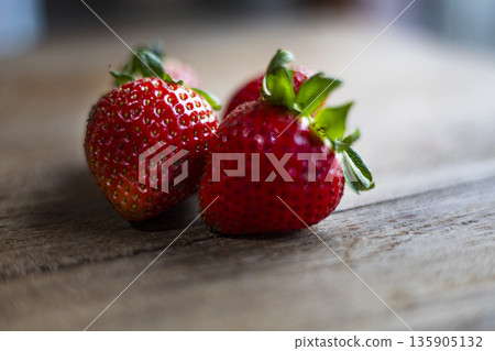 Fresh Strawberry Resting On Wooden Table, A luscious ad photo, vibrant red gleaming with tiny seeds in natural light, for a berry delight campaign or a rustic harvest documentary. 135905132