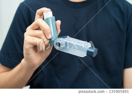 Asthma and chronic obstructive pulmonary disease COPD, Asian young man using metered dose inhaler MDI. 135905891