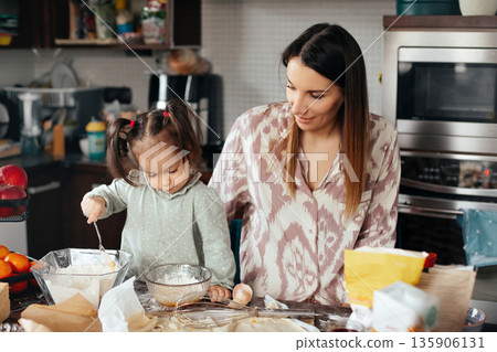 Mom and daughter make cookies together in a kitchen full of baking supplies and fresh ingredients during a weekend afternoon Mom and daughter make cookies together in a kitchen full of baking supplies and fresh ingredients during a weekend afternoon 135906131