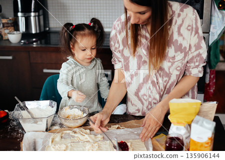 Mom and daughter make dough and cook together in the kitchen during the afternoon while creating a family recipe with joy and fun Mom and daughter make dough and cook together in the kitchen during the afternoon while creating a family recipe with joy and fun 135906144