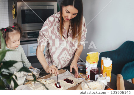 Woman prepares dough with her child by her side in a kitchen during the afternoon, enjoying a baking activity together with various ingredients around 135906145