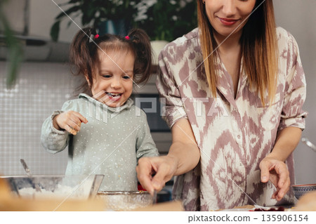 Mother and child work together in the kitchen making dessert on a sunny afternoon while sharing smiles and laughter Mother and child work together in the kitchen making dessert on a sunny afternoon while sharing smiles and laughter 135906154