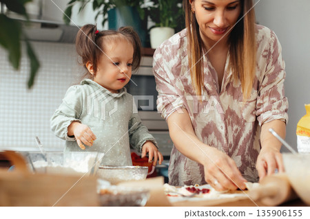 Mother and child making food together in a kitchen during daytime while having fun and sharing an enjoyable moment with ingredients on the counter Mother and child making food together in a kitchen during daytime while having fun and sharing an enjoyable moment with ingredients on the counter 135906155