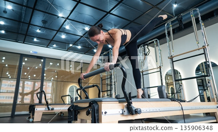 Caucasian woman doing exercises on reformer machine. Caucasian woman doing exercises on reformer machine. 135906348